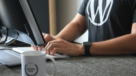 Pessoa a trabalhar ao computador com uma t-shirt com o logótipo do WordPress